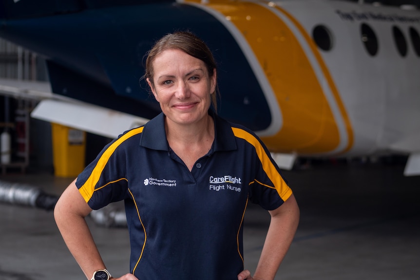 A woman in short sleeve polo work shirt beside a small plane in a hanger.