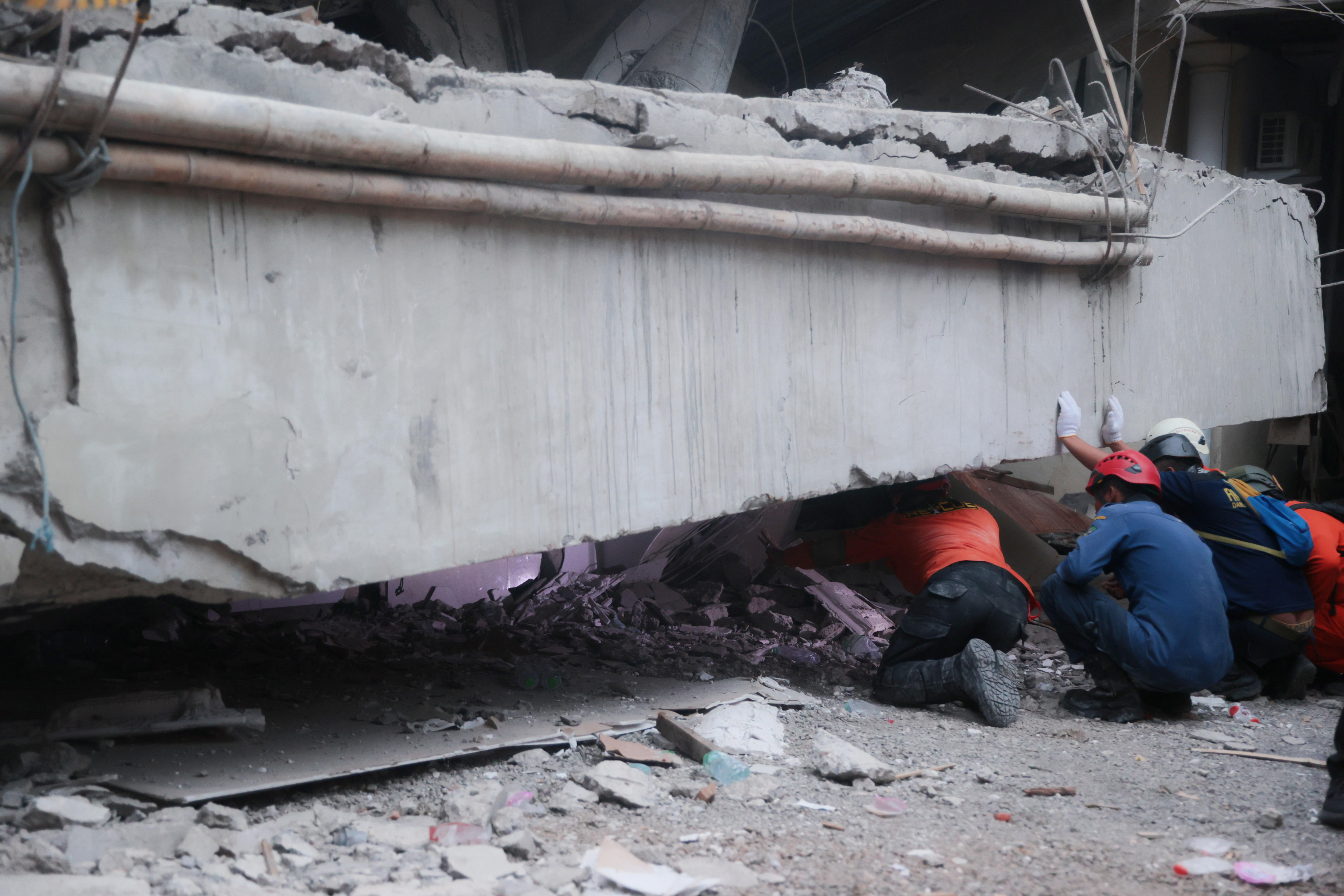 Rescuers look and crawl under a huge slab of concrete as they search for victims.