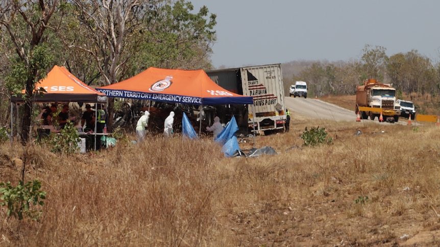 Scene of car crash with investigators under a tent near a crashed truck and car near bush on side of road