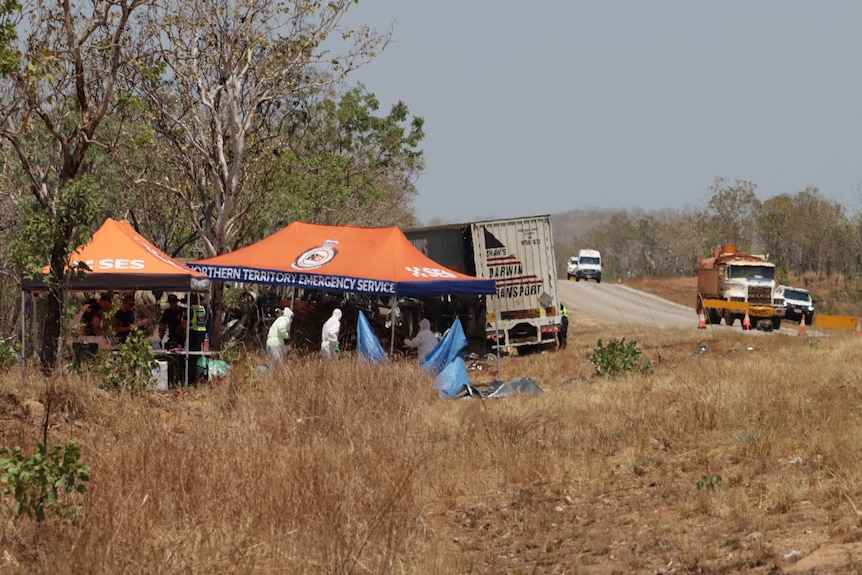 Scene of car crash with investigators under a tent near a crashed truck and car near bush on side of road