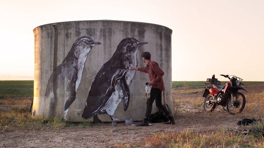 Concrete tank with large murals of penguins being painted on it.
