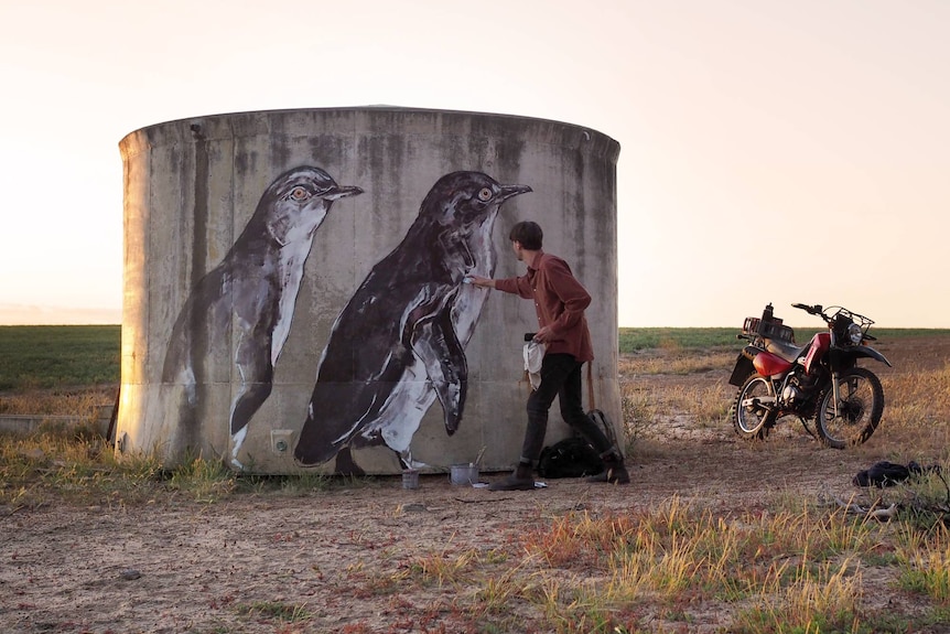 Concrete tank with large murals of penguins being painted on it.