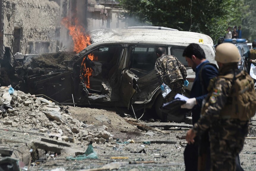 Afghan security forces inspect a damaged vehicle at the site of a suicide bombing