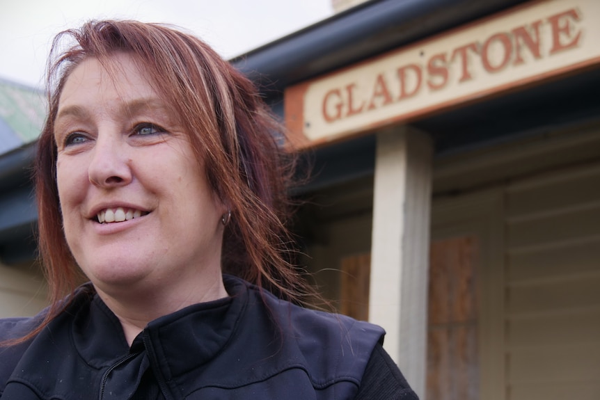 A woman looking into the distance in foreground, sign on building saying 'Gladstone' behind.