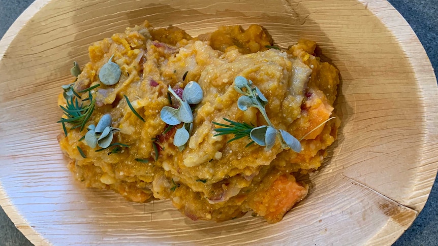 A rich yellow vegetable stew topped with garnishing leaves in a wooden dish.