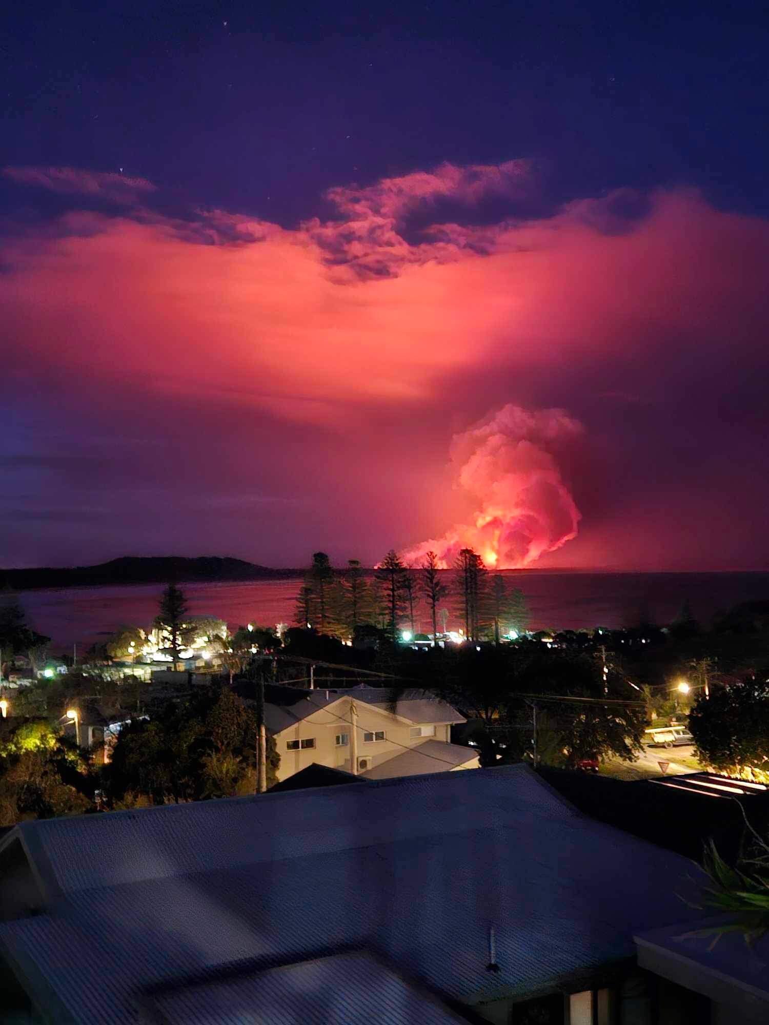 A huge ball of flames and smoke rises in the distance acoss a body of water near Kempsey in NSW