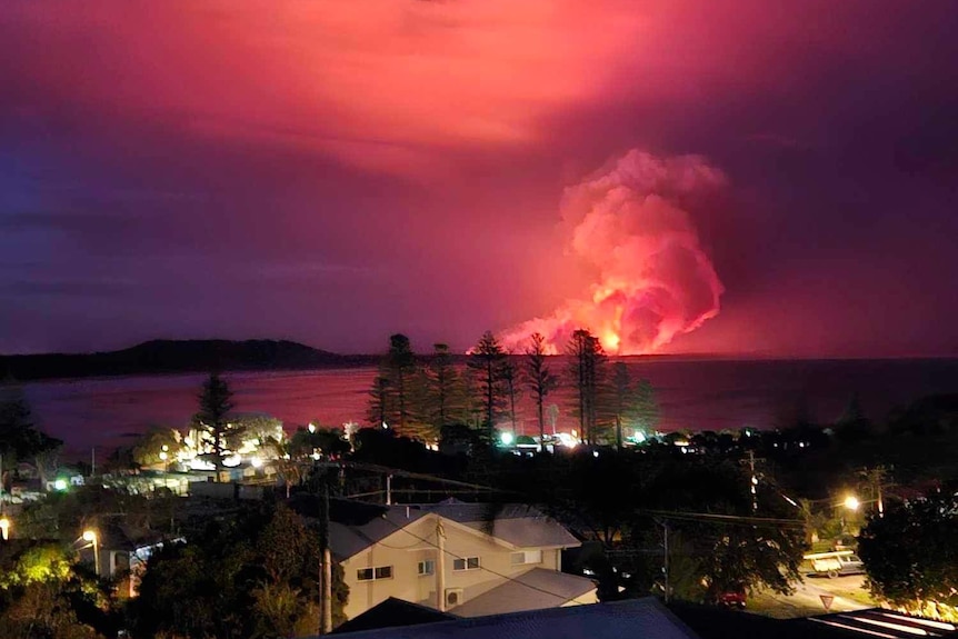 A huge ball of flames and smoke rises in the distance acoss a body of water near Kempsey in NSW