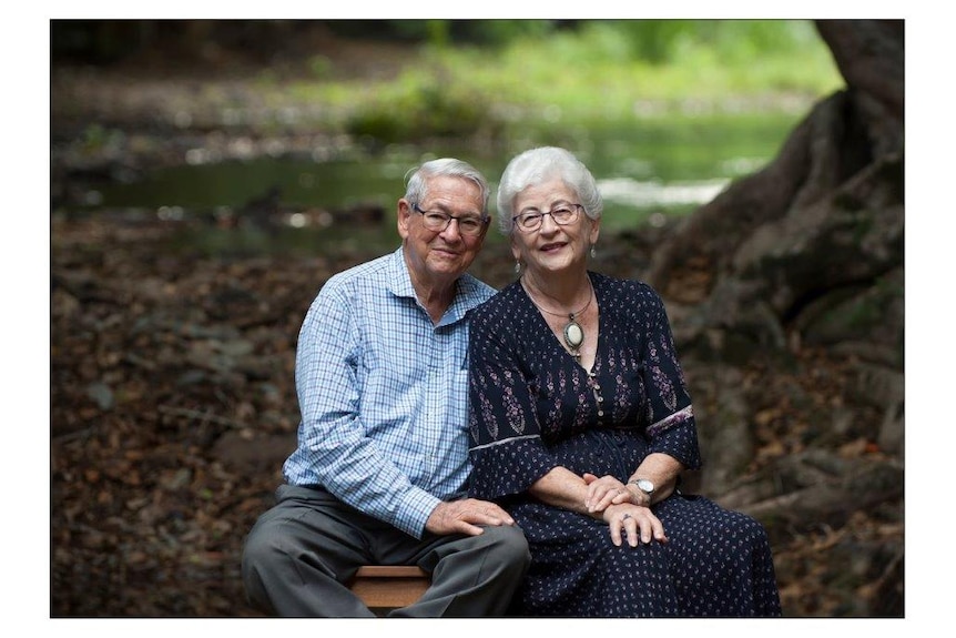 An elderly couple sit together for a portrait in a garden.