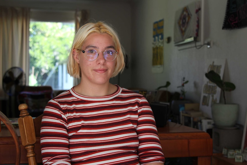 Mary Clare smiles, sitting in her home. She has blonde hair and glasses.