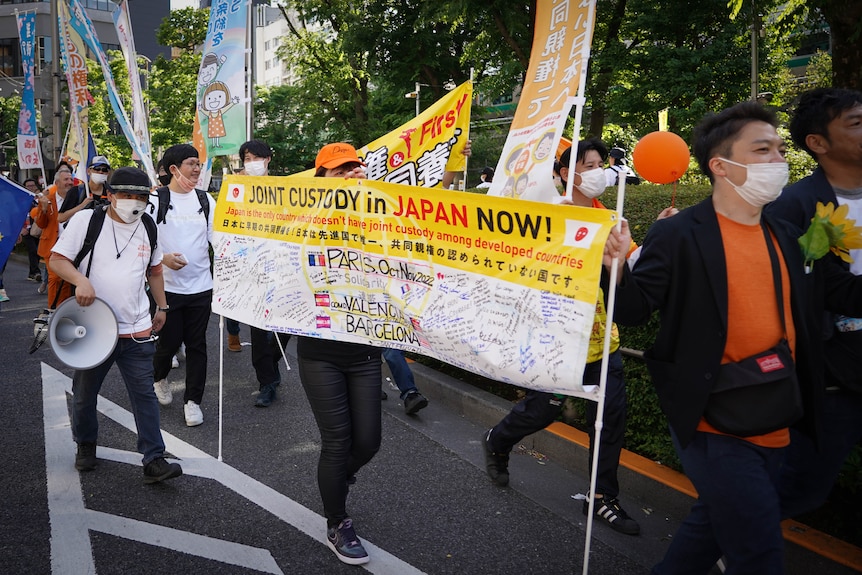 Protesters march in Japan, holding a sign reading "Joint Custody in Japan Now" 