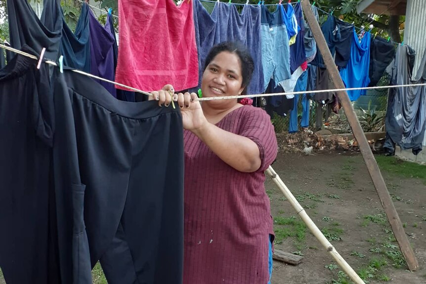 A Tongan woman hangs clothing on a washing line outside. 