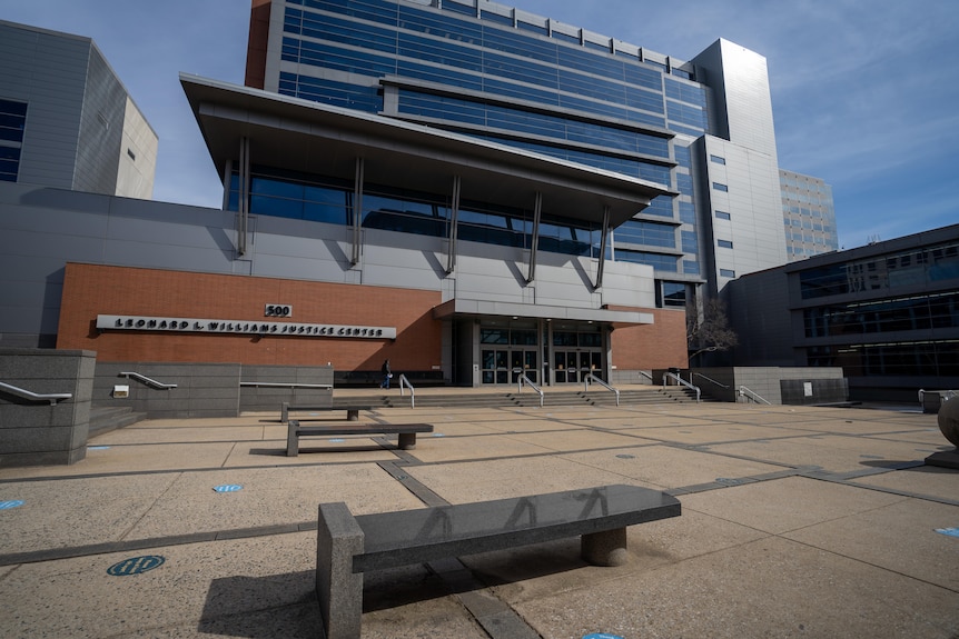 The exterior of a court building, consisting of red brick and grey metal, with a paved courtyard in front