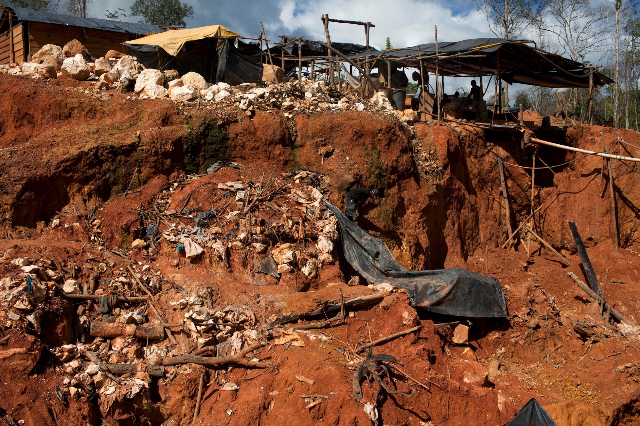 A large mound of orange clay dirt, with erosion and dig marks, cluttered by rocks and stones.