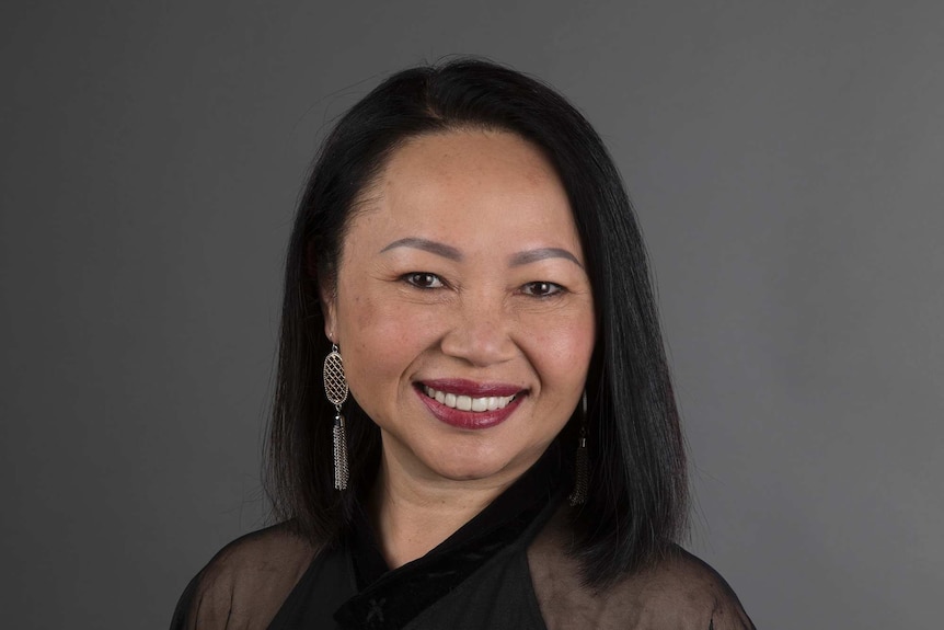 Carina Hoang, who plays Iris in the TV show The Heights, smiling at the camera in front of a grey background.