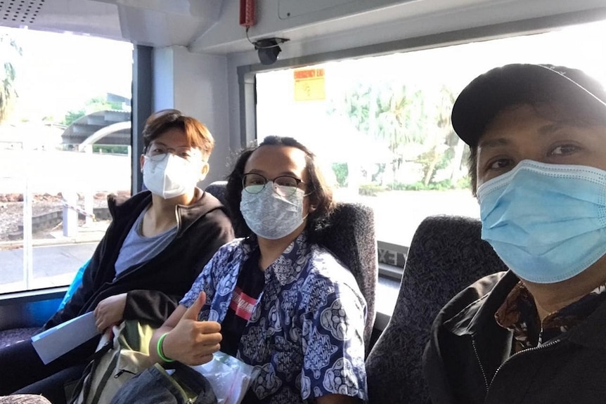 Three students wearing face masks look at the camera while sitting on a bus..