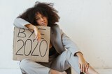 A woman slumped over a sign that says 'Bye 2020'.