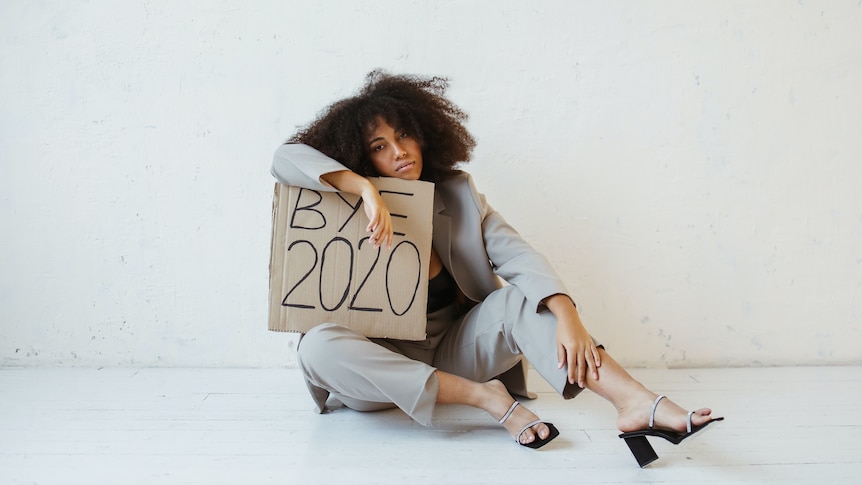 A woman slumped over a sign that says 'Bye 2020'.