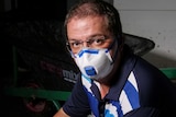 A man looks up at the camera, wearing a face mask, in a flood-affected room.