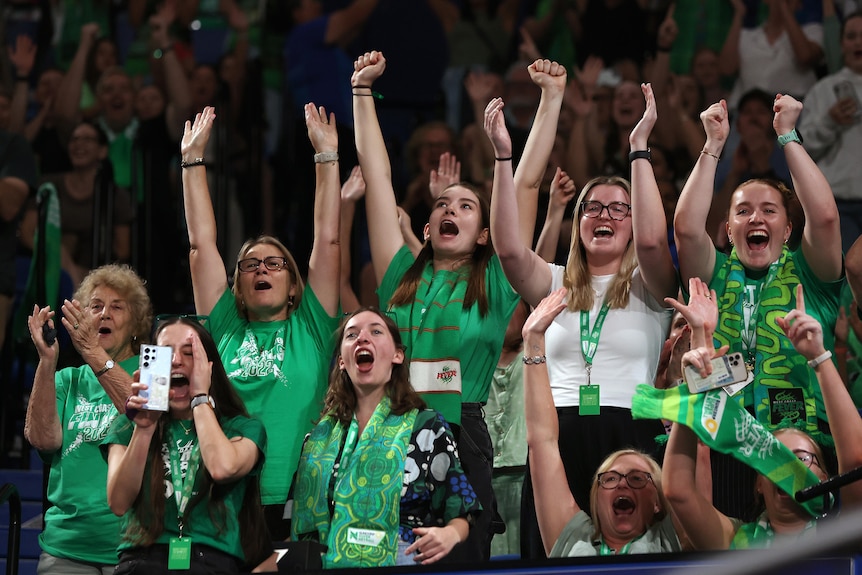 Fans wear green West Coast Fever merch as they cheer with their hands in the air