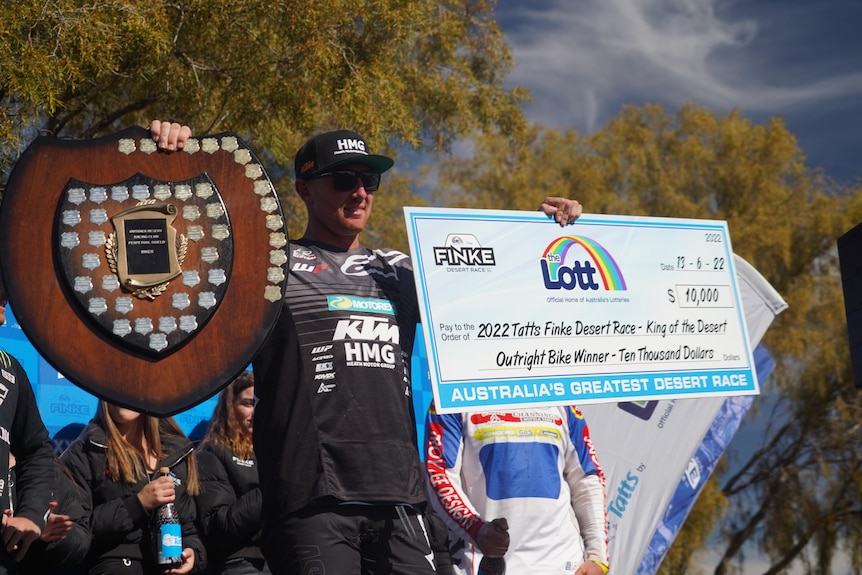 man in dirt bike racing clothes holding cheque and plaque