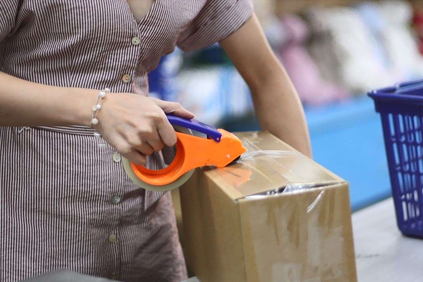 Angela uses sticky tape to pack her boxes in a daigou shop.