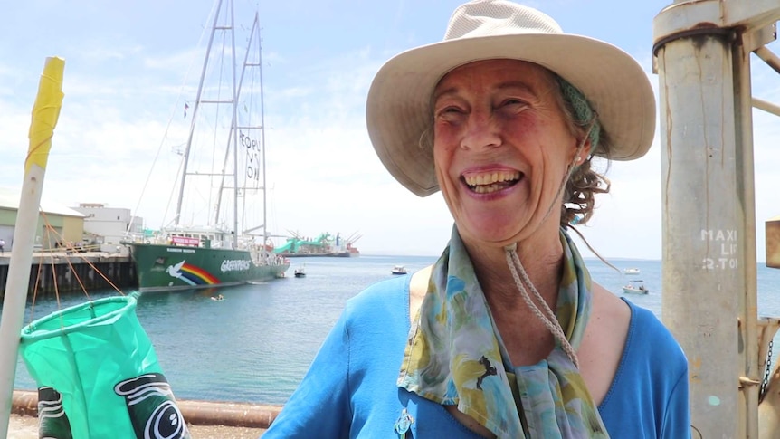 Woman wearing hat standing on wharf with Rainbow Warrior on the left background