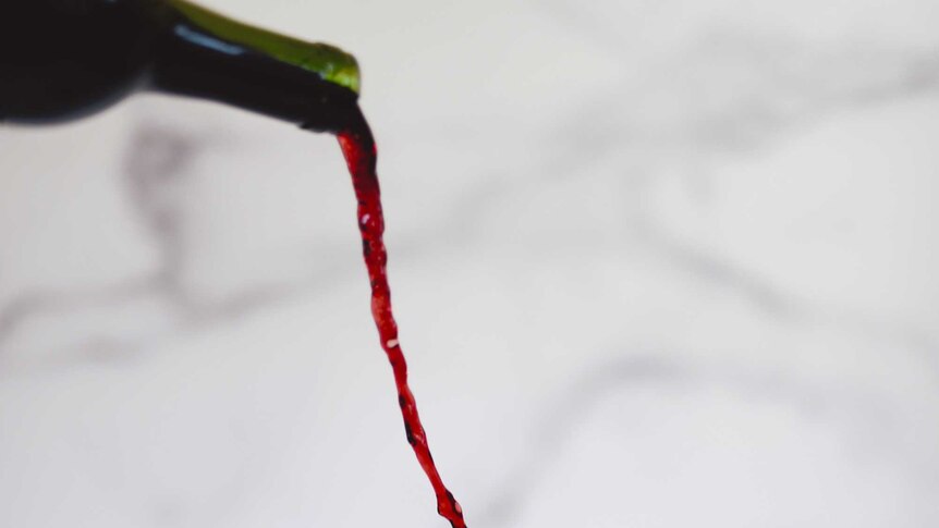 Wine is poured from up high into a glass, splashing at the edges.