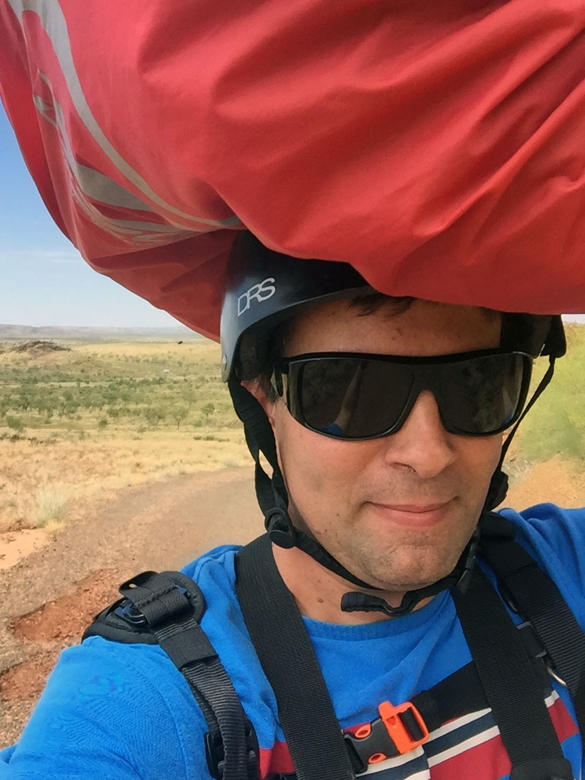 Damian Gribble walking up Telstra Hill with his paragliding gear resting on his head.