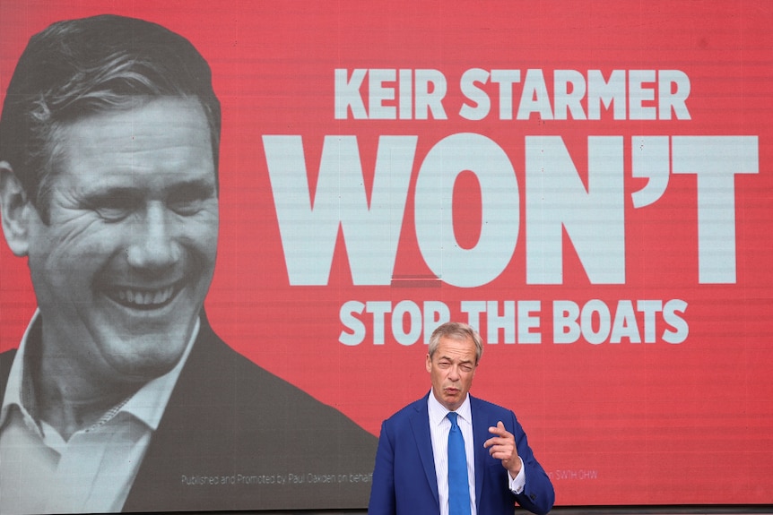 Nigel Farage stands under giant sign saying Keir Starmer Won't Stop The Boats