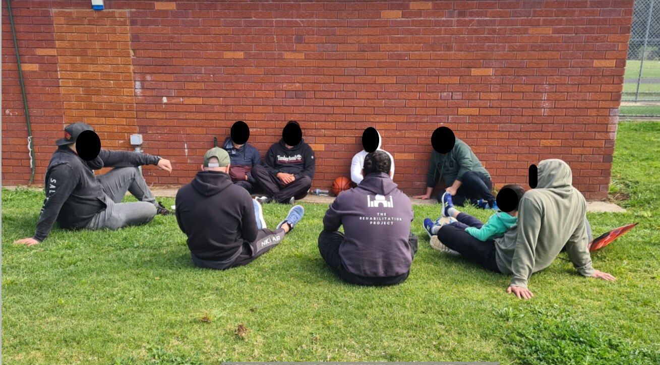 A group of men with their face blurred sitting on grass