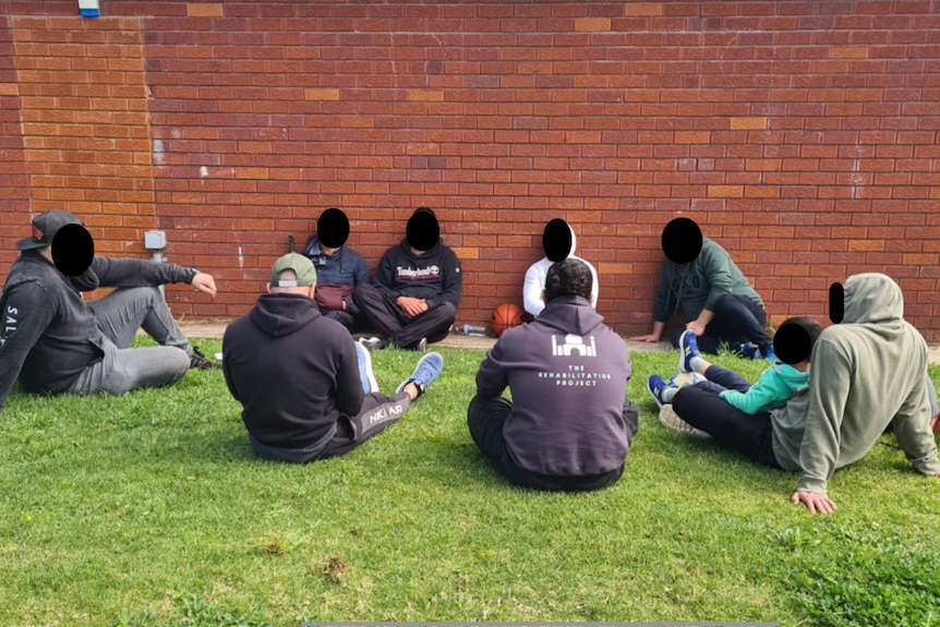 A group of men with their face blurred sitting on grass
