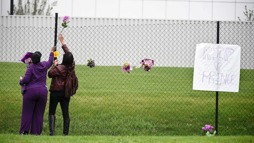 Prince fans leave flowers outside Paisley Park next to a sign remembering Prince.
