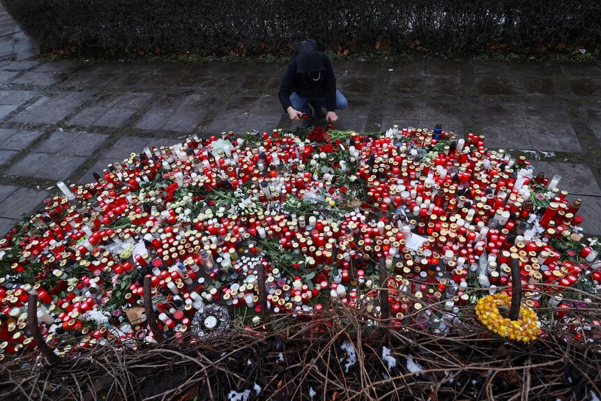 A person knealing in front of a pile of candles and flowers. 