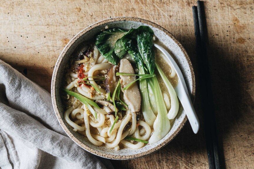 A bowl of udon noodle soup with baby bok choy, sliced shiitake mushrooms and spice, a quick and easy vegetarian recipe.
