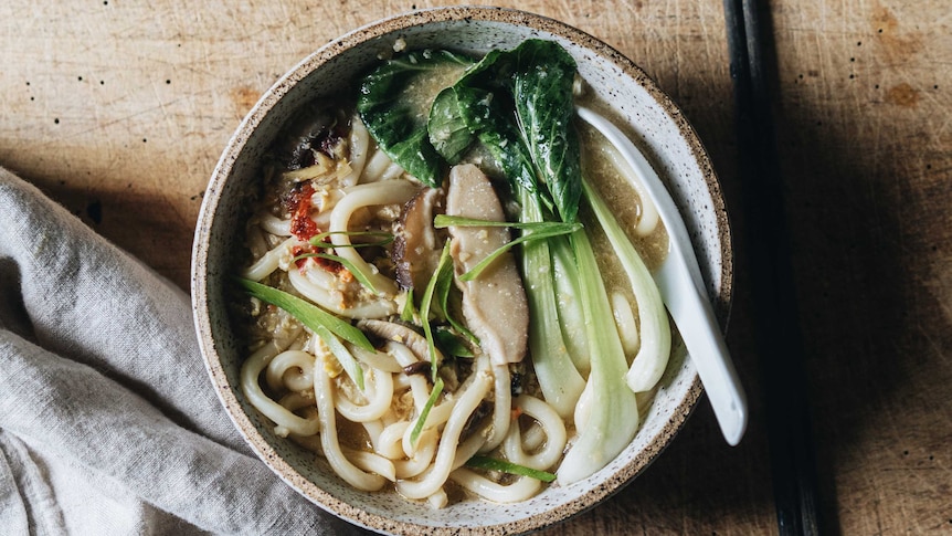 A bowl of udon noodle soup with baby bok choy, sliced shiitake mushrooms and spice, a quick and easy vegetarian recipe.