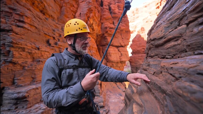 Dr Tim Flannery hangs while abseiling against a red rock cliff