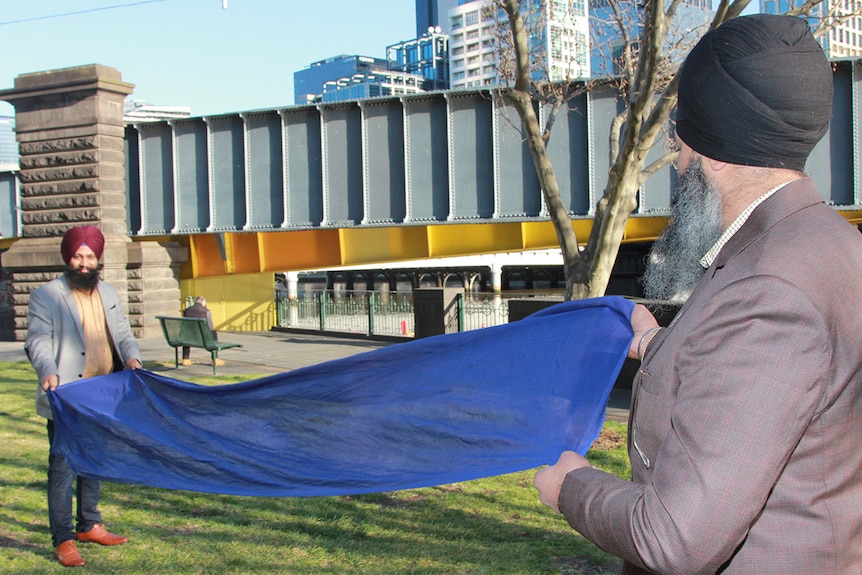 Amar Singh and Sabhi Singh stretch out the blue material used to tie a turban.