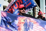 A man holds a flag showing an image of Donald Trump in front of the American flag with an explosion in the background.