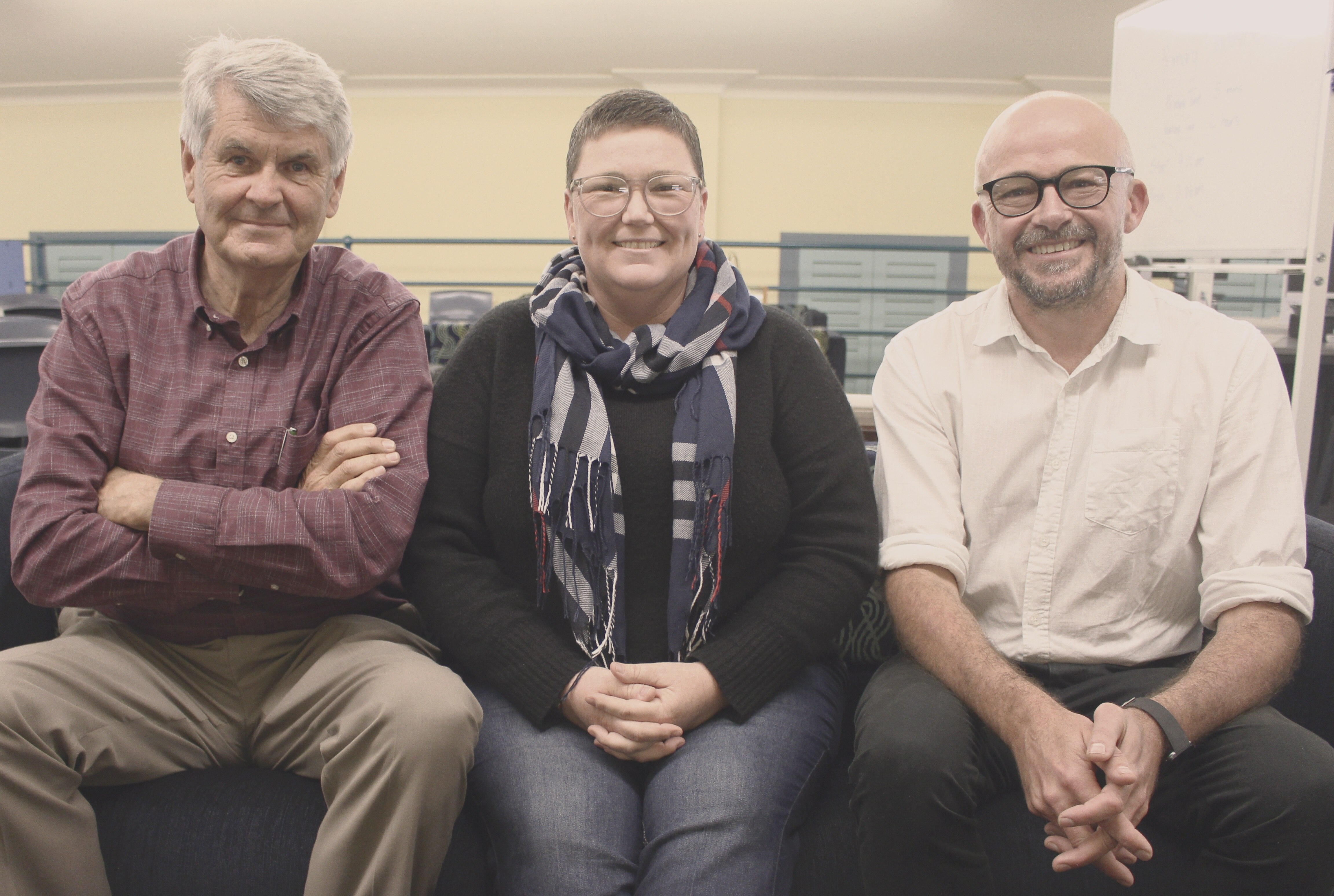 Two men and a woman sit in a library, posing for a photo.