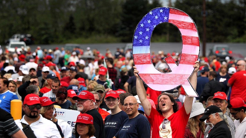 David Reinert holds up a large "Q" sign with American flag imagery