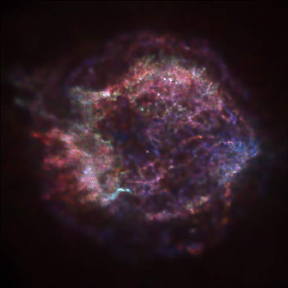 A grainy image of the  Cassiopeia A, with mostly pink colouring and few flecks of light and cobalt blue. 