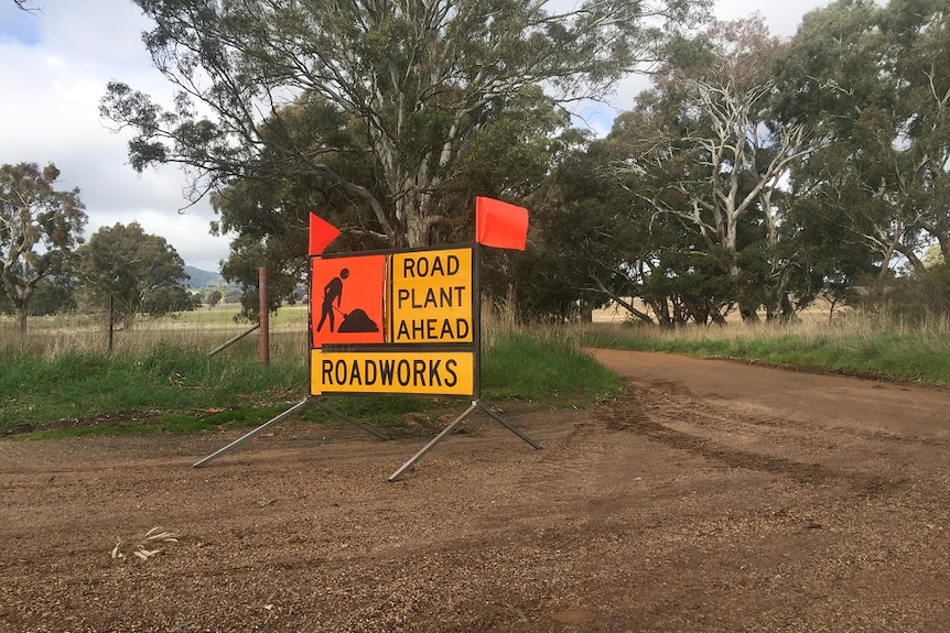 a sign set on a gravel road indicates road works are taking place ahead.