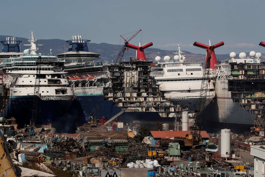 the hull of cruise ships docked together are ripped open as workers work to dismantle them