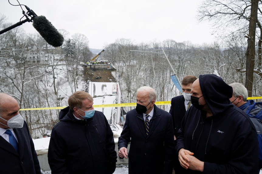 people in a press conference standing with collapsed bridge behind them