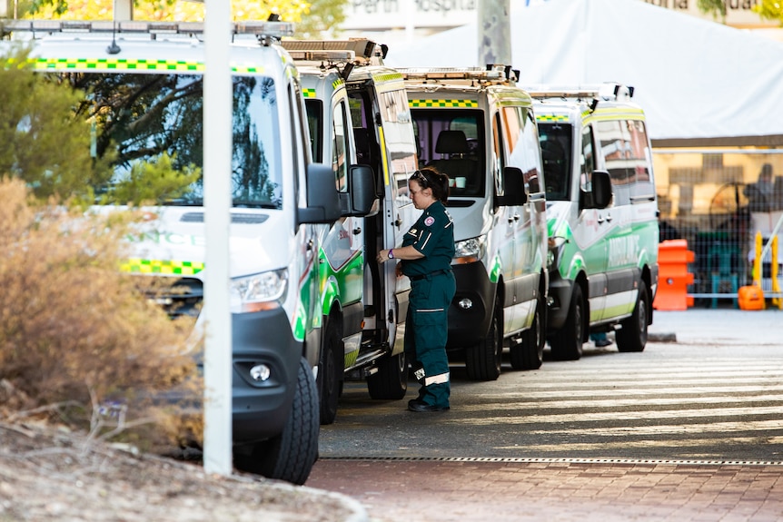 A paramedic standing alongside a parked ambulance outside a hospital.