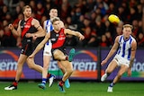 An Essendon AFL player snaps a kick towards goal as North Melbourne defenders react.