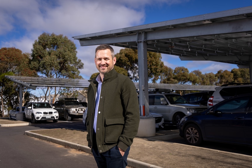 A man in a green coat standing in front of a car park with solar panel shelter