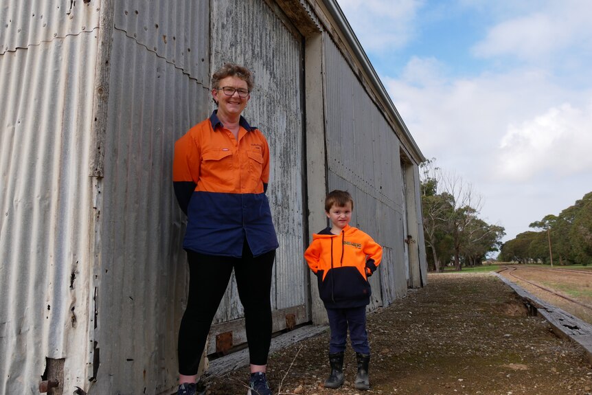A woman and her grandson stand next to an old tin building