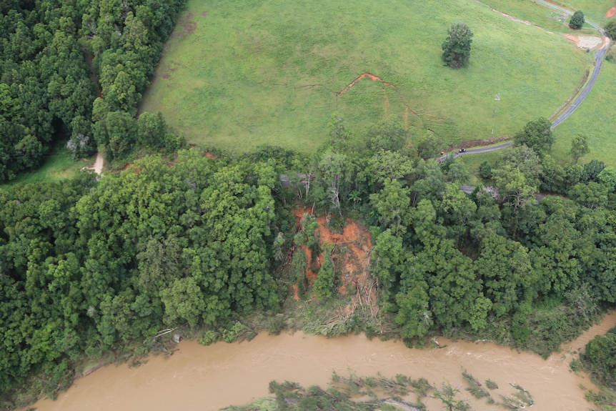 An aerial shot of a road and trees and a brown river with a landslip