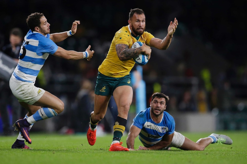 Quade Cooper runs past two Argentine players with the ball held to his chest with his eight forearm.
